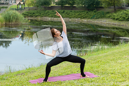 Image of Young beautiful woman doing yoga exercise in green park. Healthy lifestyle and fitness concept.