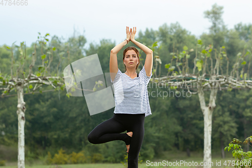 Image of Young beautiful woman doing yoga exercise in green park. Healthy lifestyle and fitness concept.