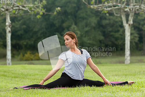 Image of Young beautiful woman doing yoga exercise in green park. Healthy lifestyle and fitness concept.