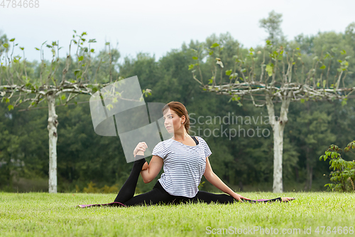 Image of Young beautiful woman doing yoga exercise in green park. Healthy lifestyle and fitness concept.