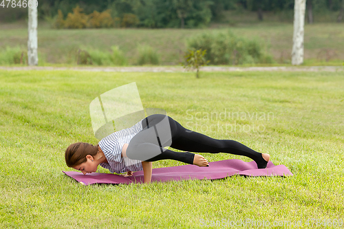 Image of Young beautiful woman doing yoga exercise in green park. Healthy lifestyle and fitness concept.