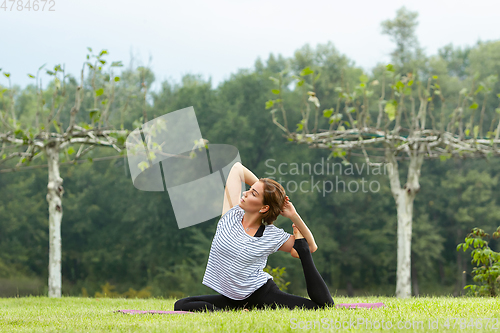 Image of Young beautiful woman doing yoga exercise in green park. Healthy lifestyle and fitness concept.