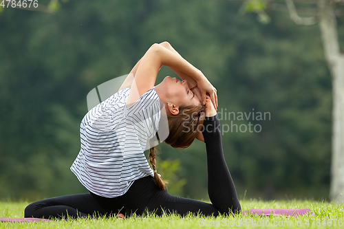 Image of Young beautiful woman doing yoga exercise in green park. Healthy lifestyle and fitness concept.