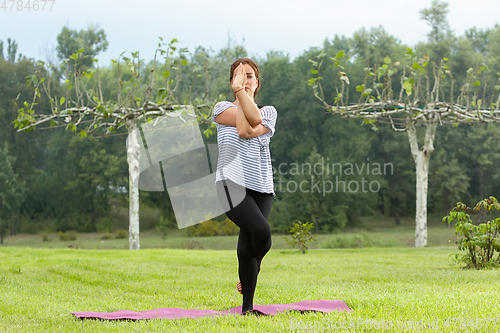 Image of Young beautiful woman doing yoga exercise in green park. Healthy lifestyle and fitness concept.