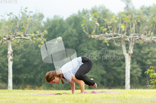 Image of Young beautiful woman doing yoga exercise in green park. Healthy lifestyle and fitness concept.