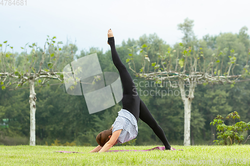 Image of Young beautiful woman doing yoga exercise in green park. Healthy lifestyle and fitness concept.