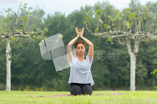 Image of Young beautiful woman doing yoga exercise in green park. Healthy lifestyle and fitness concept.