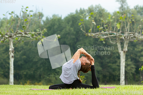 Image of Young beautiful woman doing yoga exercise in green park. Healthy lifestyle and fitness concept.