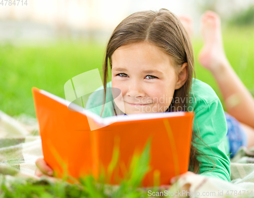 Image of Little girl is reading a book outdoors