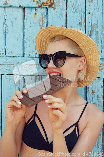 Image of Young attractive woman in sunglasses and in straw hat eating chocolate on a blue background. Film efect