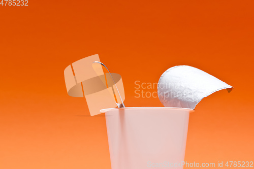 Image of empty clean yogurt cup with spoon on an orange background