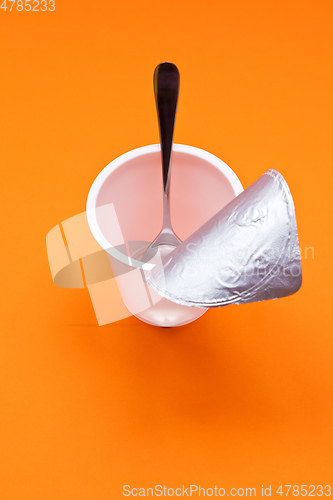 Image of empty clean yogurt cup with spoon on an orange background