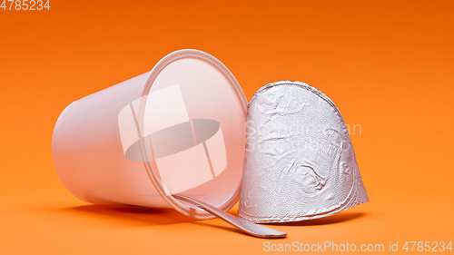 Image of empty clean yogurt cup with spoon on an orange background