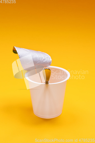 Image of empty clean yogurt cup with spoon on an orange background