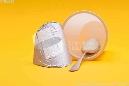 Image of empty clean yogurt cup with spoon on an orange background