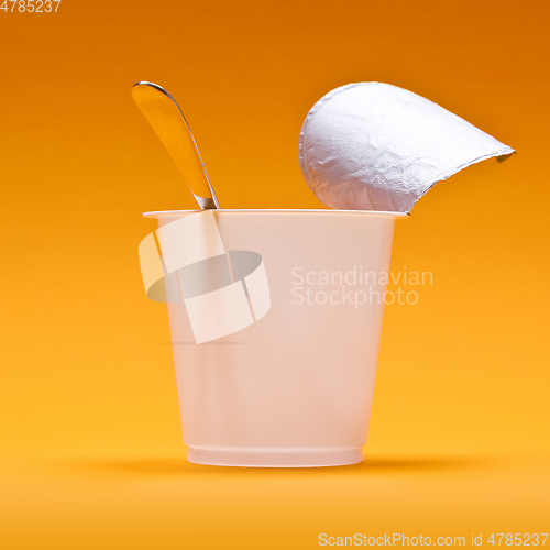 Image of empty clean yogurt cup with spoon on an orange background