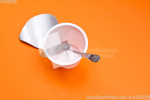 Image of empty clean yogurt cup with spoon on an orange background