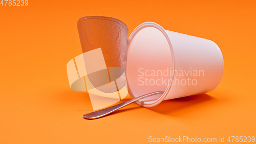 Image of empty clean yogurt cup with spoon on an orange background