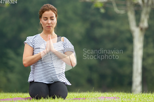 Image of Young beautiful woman doing yoga exercise in green park. Healthy lifestyle and fitness concept.