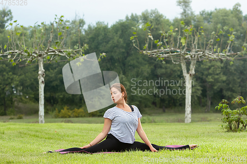 Image of Young beautiful woman doing yoga exercise in green park. Healthy lifestyle and fitness concept.