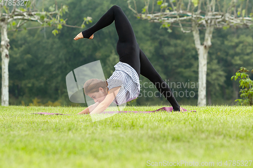 Image of Young beautiful woman doing yoga exercise in green park. Healthy lifestyle and fitness concept.