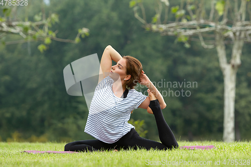 Image of Young beautiful woman doing yoga exercise in green park. Healthy lifestyle and fitness concept.