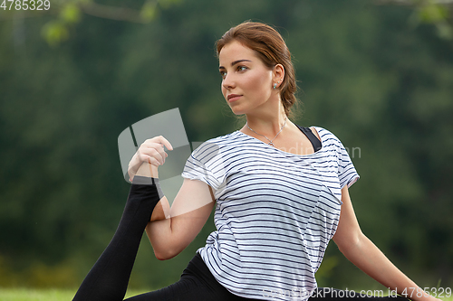 Image of Young beautiful woman doing yoga exercise in green park. Healthy lifestyle and fitness concept.