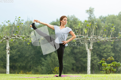 Image of Young beautiful woman doing yoga exercise in green park. Healthy lifestyle and fitness concept.