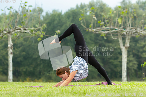 Image of Young beautiful woman doing yoga exercise in green park. Healthy lifestyle and fitness concept.