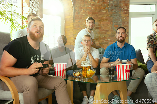 Image of Group of excited friends playing video games at home