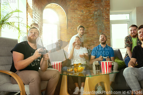 Image of Group of excited friends playing video games at home