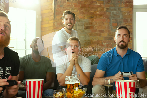 Image of Group of excited friends playing video games at home