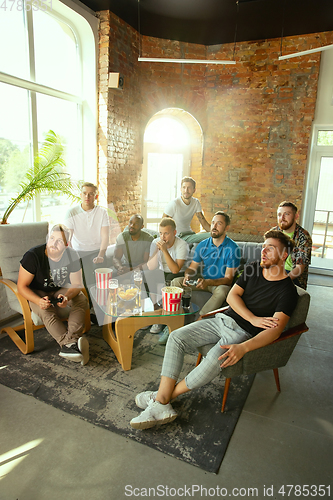 Image of Group of excited friends playing video games at home