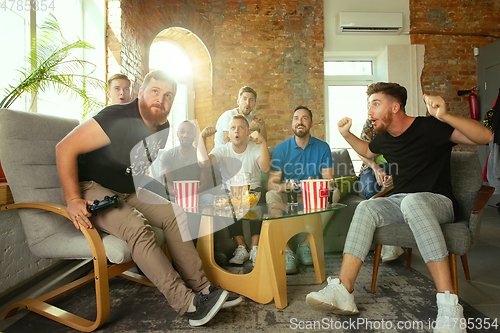 Image of Group of excited friends playing video games at home