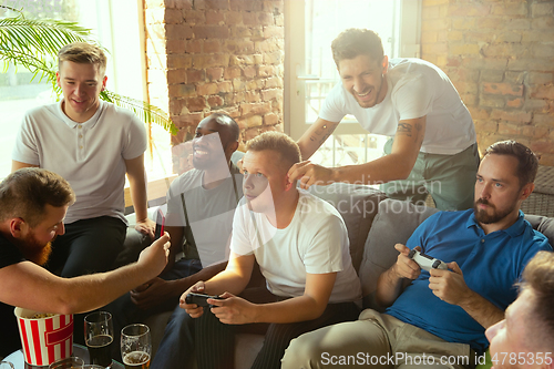 Image of Group of excited friends playing video games at home