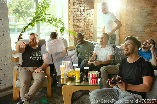 Image of Group of excited friends playing video games at home