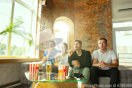 Image of Group of friends watching football or soccer game on TV at home