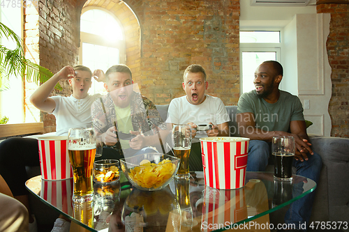 Image of Group of excited friends playing video games at home