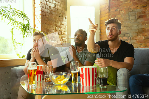 Image of Group of friends watching football or soccer game on TV at home