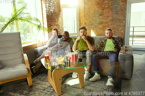 Image of Group of friends watching football or soccer game on TV at home