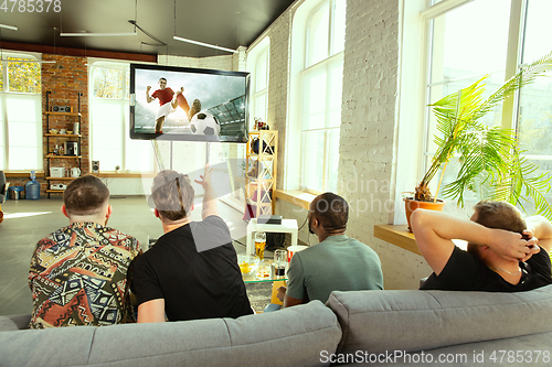 Image of Group of friends watching football or soccer game on TV at home