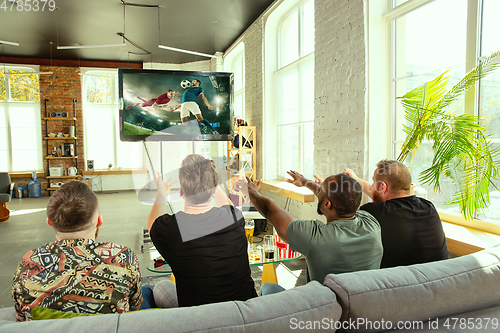 Image of Group of friends watching football or soccer game on TV at home