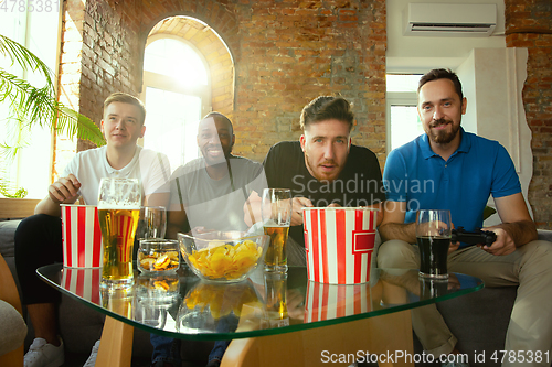 Image of Group of excited friends playing video games at home