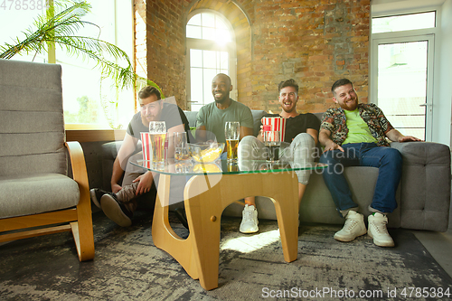 Image of Group of friends watching football or soccer game on TV at home