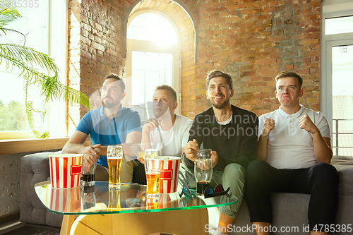 Image of Group of friends watching football or soccer game on TV at home