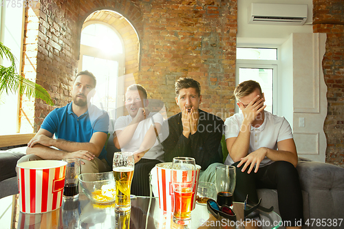 Image of Group of friends watching football or soccer game on TV at home