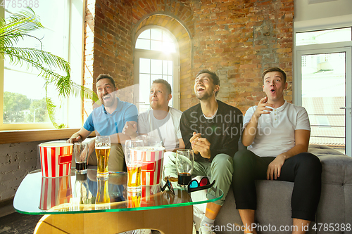 Image of Group of friends watching football or soccer game on TV at home