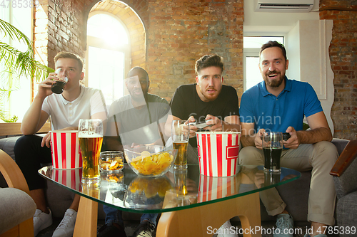 Image of Group of excited friends playing video games at home