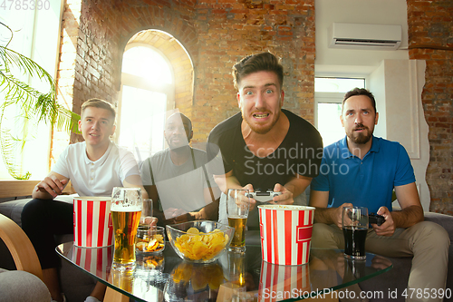 Image of Group of excited friends playing video games at home