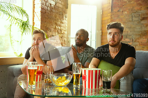 Image of Group of friends watching football or soccer game on TV at home